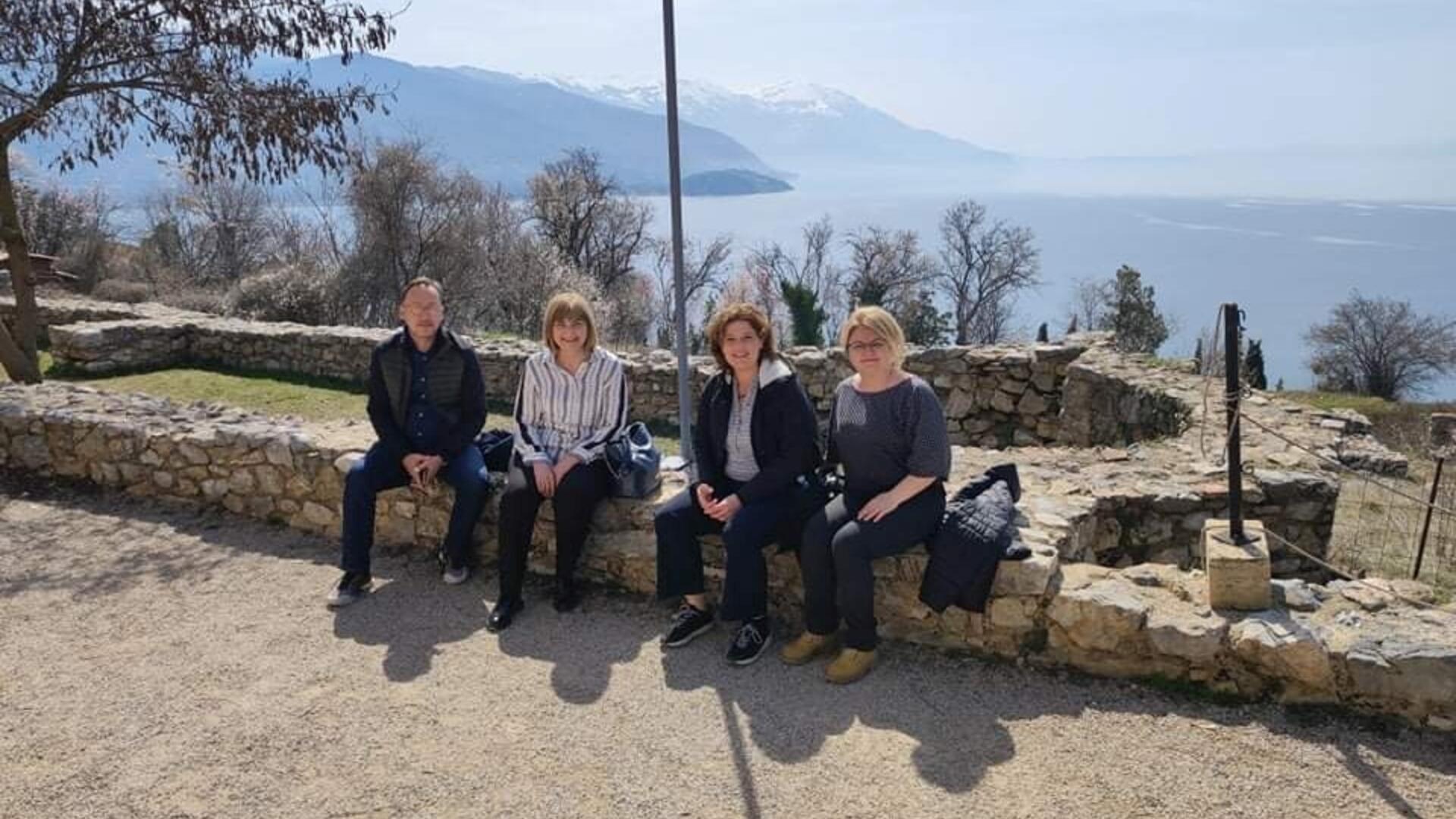 Group picture of 4 people including Gebke, sitting on the shore of lake Ohrid